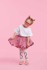 Happy childhood. Funny child girl in tulle skirt jumping and having fun isolated on pink background. Celebrating a vibrant carnival for kids, birthday party. True emotions. Space for text