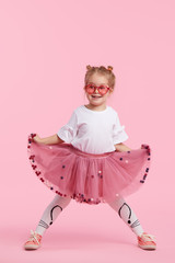 Happy childhood. Funny child girl in tulle skirt jumping and having fun isolated on pink...
