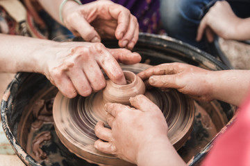 A close up view on ceramic production process on potter's wheel with children. Clay crafts with kids concept.