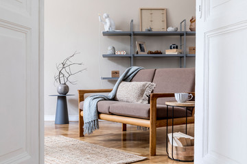 Modern interior design of living room with brown wooden sofa, gray bookstand, vase with flowers, coffee table, decoration and elegant accessories. Beige and japandi concept. Stylish home staging. 