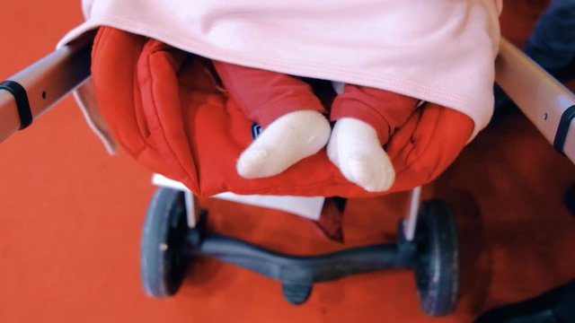 Newborn baby girl swinging her feet while sleeping in a stroller, top view