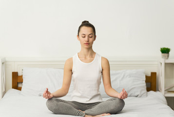 Meditation. Millennial woman sitting in lotus position on bed