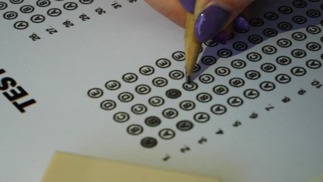 Female student hand testing doing examination test with standardized test form and answers bubbled. Student filling out answers.