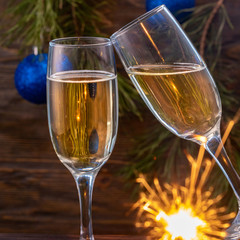 Glasses of champagne with bubbles on the background of Christmas decorations. Glasses touch during a festive toast and sparklers burn beautifully. Beautiful card. Square.