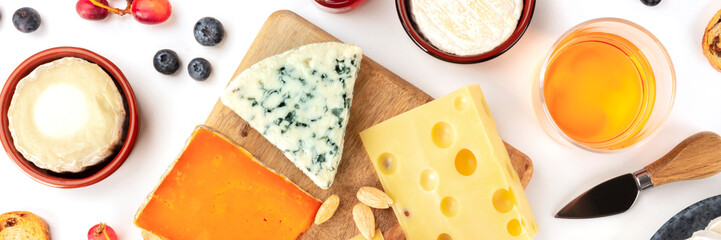 Cheese platter flatlay panorama on a white background. Blue cheese, red, goat cheese, and others,...