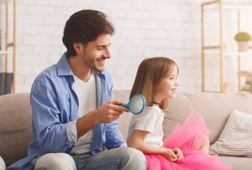 Handsome young father combing his little daughter hair