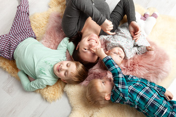 Top view of beautiful young mother, their cute little daughter and two son, lying on wooden floor.