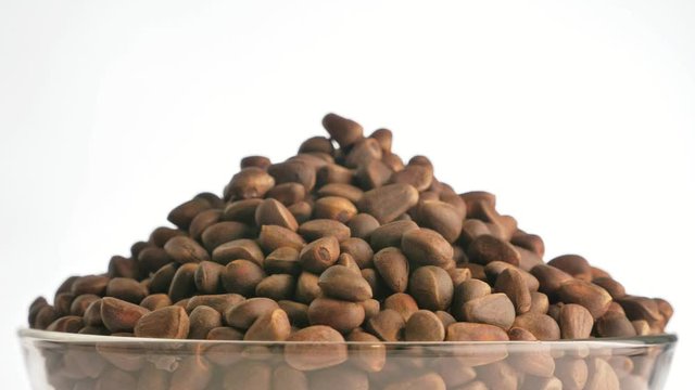 Pine nut rotate are on a table in a plate. Snack in transparent dish on an isolated white background are spinning moving. Delicious and healthy protein-rich diet food.