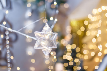 Fototapeta premium Transparent toy star on Merry Christmas or New Year background. Warm golden lights and bokeh. Shiny sparkling garlands. Copy space.