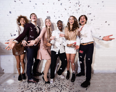 Millennials Standing Showered With Confetti Celebrating Against White Wall Indoor