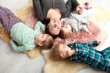 Top view of beautiful young mother, their cute little daughter and two son, lying on wooden floor.