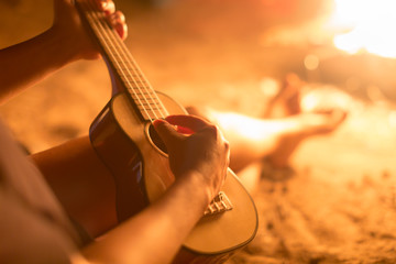 A female musician playing guitar outside, sitting next to a fire. Relaxation.