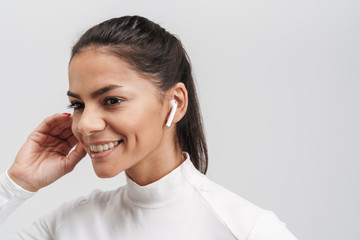 Image of young brunette woman in sportswear putting on earpods isolated over gray background