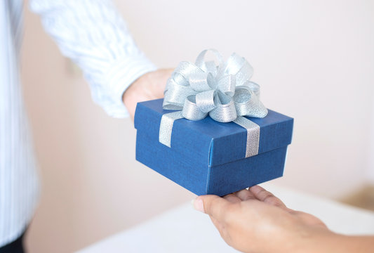 Close up of young man give a gift in a box,holding blue Gift box with bow over holiday background which celebrating  couple image