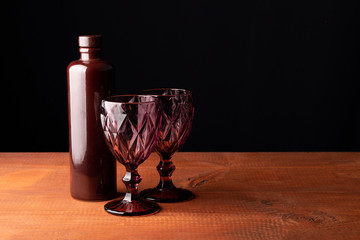 Ceramic bottle of wine and two red faceted glasses on a wooden table.