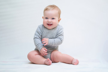  A 6 month old baby learns to sit down. photo on a neutral background