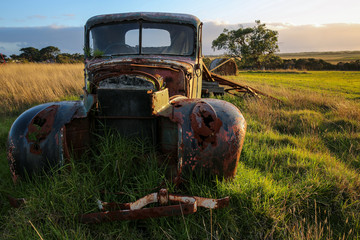 The rusting hulk of an abandoned old truck, overgrown by grass, sit forlorn in a field.