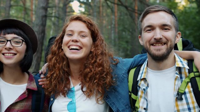 Portrait of laughing girls and guys friends in the woods having fun hugging looking at camera standing in green forest. Emotions and active lifestyle concept.