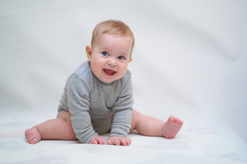  A 6 month old baby learns to sit down. photo on a neutral background