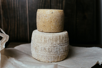 Different homemade cheeses on a dark wooden background. Pieces and cheese heads of kravot, manchego, Paramezan. Goat and cow cheese on baking paper. Handwork. Close up