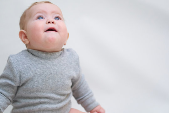  A 6 month old baby learns to sit down. photo on a neutral background