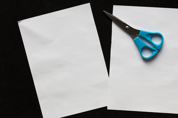 Two pieces of rectangular sheet of paper and scissors on the black background