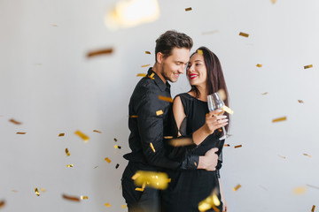 Brunette long-haired woman looks at husband's face with tenderness, enjoying birthday party. Indoor...