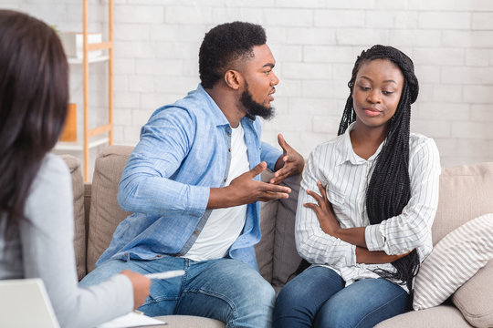 Angry black man blaming his indifferent wife during therapy counselling session