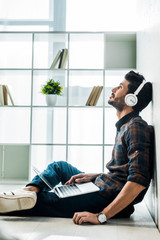 side view of handsome and smiling bi-racial man with laptop listening music