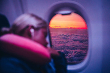 Sleeping in airplane, concept photo. Woman sleep in aircraft. Beautiful sunset sky and clouds behind the airplane window.