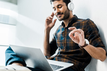 low angle view of handsome and smiling bi-racial man with laptop listening music