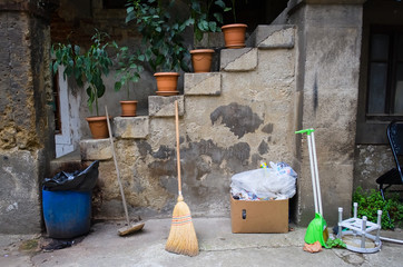 Flowerpots stairs with green flowers, broom and trash boxes in a small courtyard of old area of...
