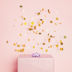 Pastel purple gift box with gold confetti stars on pink background. Holiday concept for Birthday card, Christmas, Mothers day and Wedding