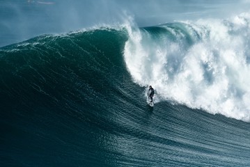 Surfer riding forward the moving foamy wave of the Atlantic Ocean at Nazare, Portugal