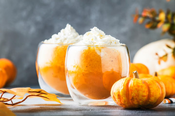 Pumpkin spiced latte or coffee in double glass cup on gray table. Autumn or winter hot drink in festive orange table setting