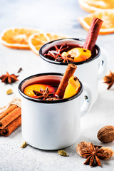 Mulled wine in white metal mugs with cinnamon, spices and orange on concrete background,...