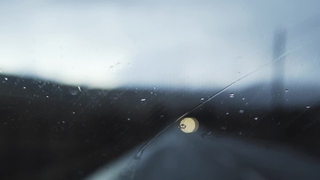 Raindrops on windshield of car with windscreen wipers, slow motion