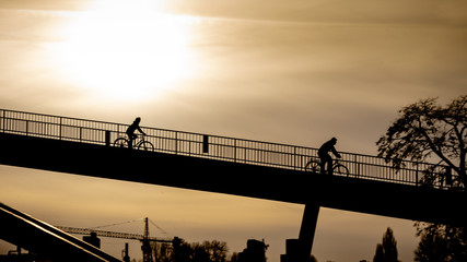 Two bike-riders driving down the bridge in the late backlight sun near Cologne