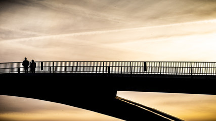Two people stay on a bridge in the late backlight sun and enjoy the landscape,