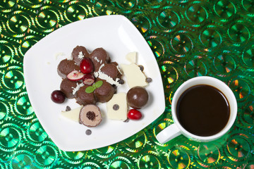 Chocolate fudge garnished with chocolate, mint and cranberries. Lies on a white plate, on a green background.