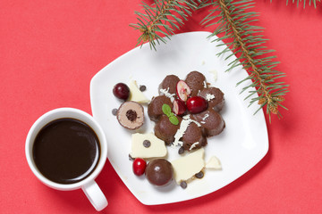 Chocolate fudge garnished with chocolate, mint and cranberries. Lies on a white plate, on a white background. Nearby a cup of coffee and a branch of spruce.