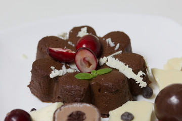 Chocolate fudge garnished with chocolate, mint and cranberries. Lies on a white plate, on a white background.