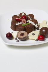 Chocolate fudge garnished with chocolate, mint and cranberries. Lies on a white plate, on a white background.