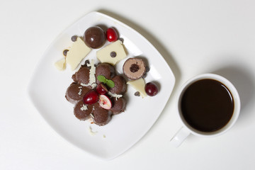 Chocolate fudge garnished with chocolate, mint and cranberries. Lies on a white plate, on a white background. Near a cup of coffee.