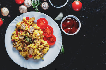 scrambled eggs with mushrooms and vegetables in white plate on dark background