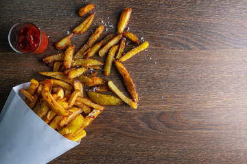 French fries in a paper bag with sauces on wooden back ground