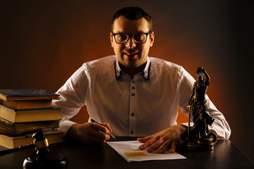 Smiling male lawyer on his desk with paperwork. Libra and wooden gavel and books