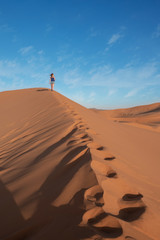 Fototapeta na wymiar Young girl walking through the dunes in sahara desert in Morocco