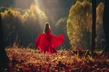 Beautiful brunette girl in a chic red dress posing in the fairy autumn forest. © kovop58