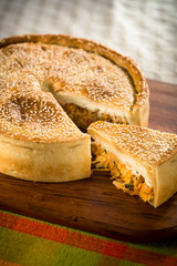 Sliced salty pie with a crispy golden-brown crust and white sesame, ready to eat, on a blue napkin